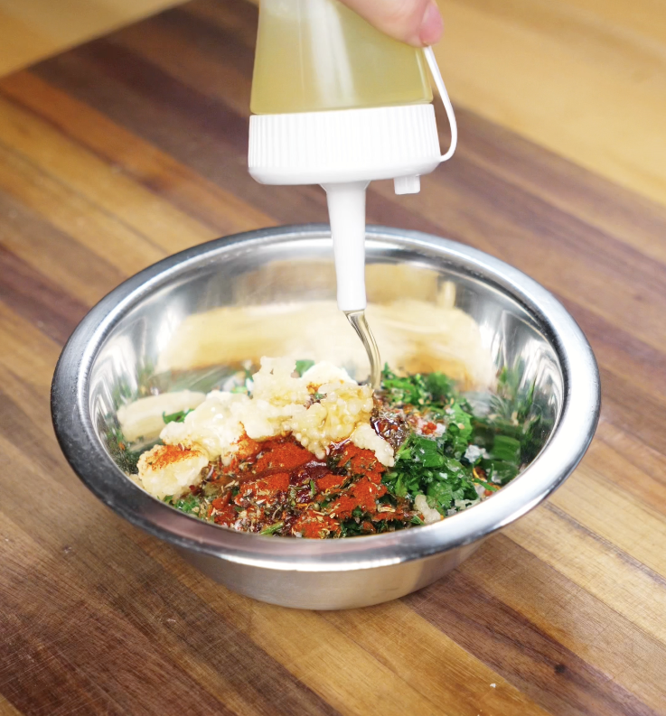 A bowl of chimichurri ingredients: parsley, garlic, chili flakes, paprika, sesame oil, and rice vinegar — being combined into a bright, savory sauce.