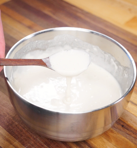 A thick, smooth batter made from flour, cornstarch, baking powder, and water being stirred until fully combined for frying the chicken.