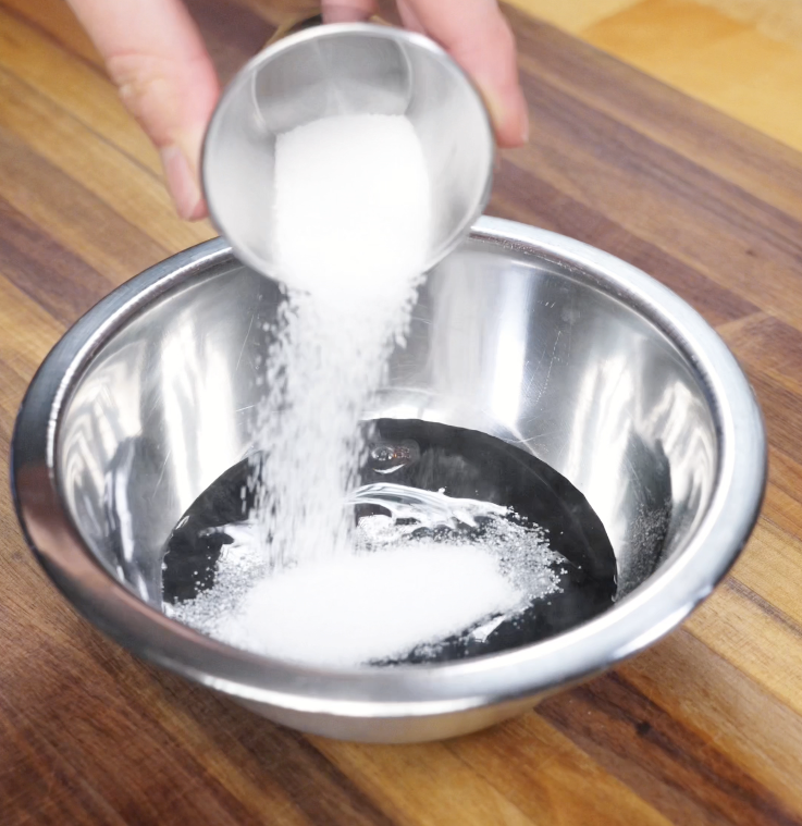 White sugar being poured into a bowl of dark soy, light soy, and oyster sauce for Shanghai noodle stir fry.