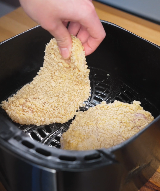 Breaded chicken cutlets being placed into an air fryer basket in a single layer, prepped for cooking until crispy and golden.