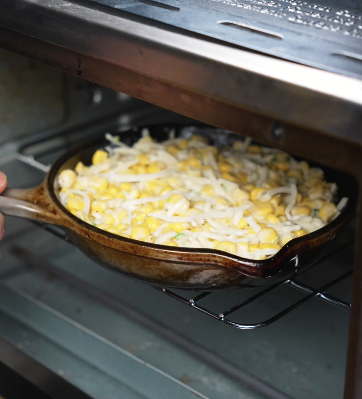 A cast iron dish filled with Korean corn cheese mixture being placed into the oven to bake until golden and bubbly.