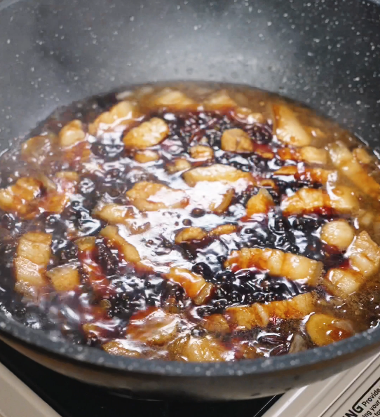 Braised pork belly simmering uncovered as the sauce reduces and thickens, turning glossy and coating each piece with a sticky soy glaze.