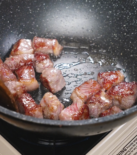 Beef cubes searing in a hot pan with oil, developing a browned crust before being removed for later stir-frying.