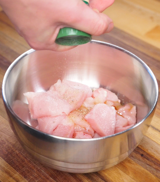 Raw chicken breast chunks being seasoned with salt, white pepper, garlic powder, and sesame oil in a mixing bowl before battering.