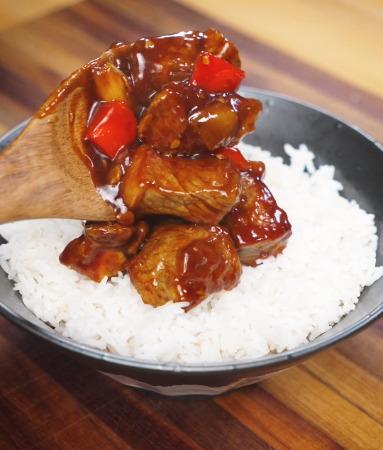 Black pepper beef being spooned over a bowl of freshly steamed white rice, with the rich sauce soaking into the grains.