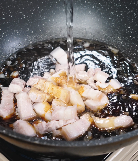 Pork belly cubes simmering in a dark soy-based braising liquid with Shaoxing wine, gently cooking until tender and infused with rich flavor.