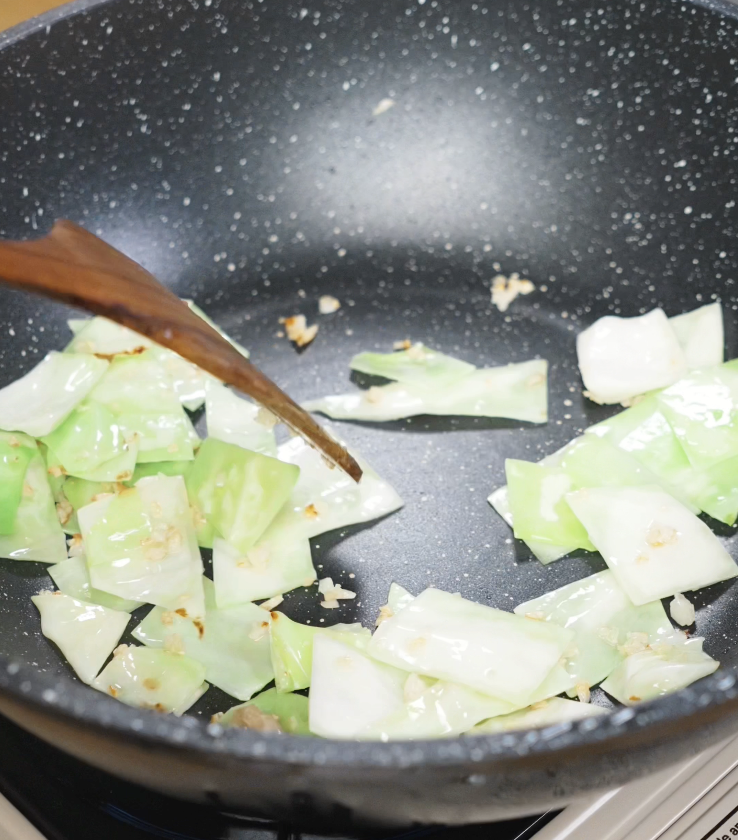 Chopped cabbage sautéing in a hot wok with garlic until slightly softened and browned.