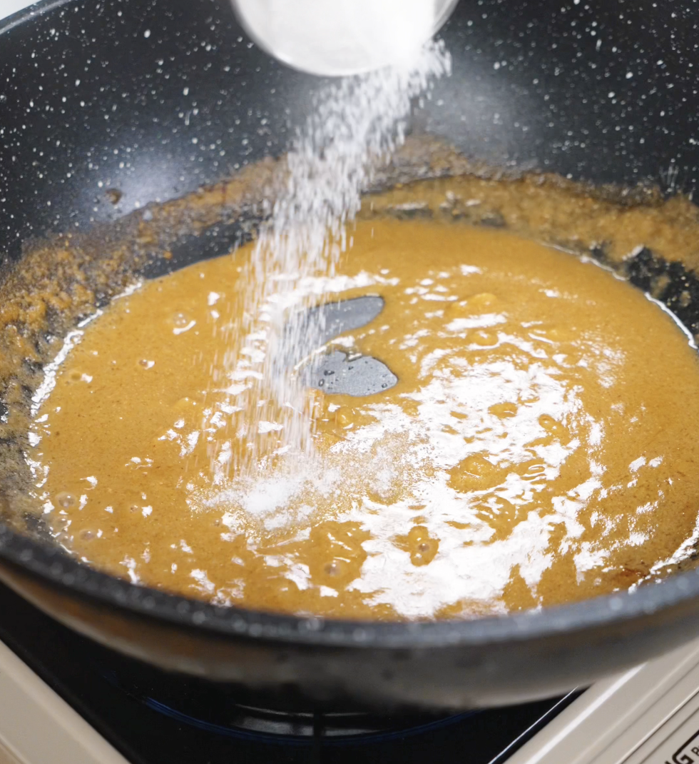 A small spoonful of sugar being mixed into the miso-butter sauce to balance the saltiness with a subtle sweetness.