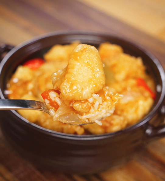 A spoonful of crispy battered chicken coated in sweet and sour sauce with rice underneath, highlighting the tangy glaze and tender interior.