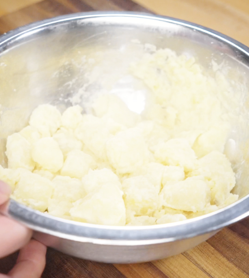 Fluffed and roughed-up boiled potatoes in a mixing bowl, prepped for ultimate crispiness in the oven.