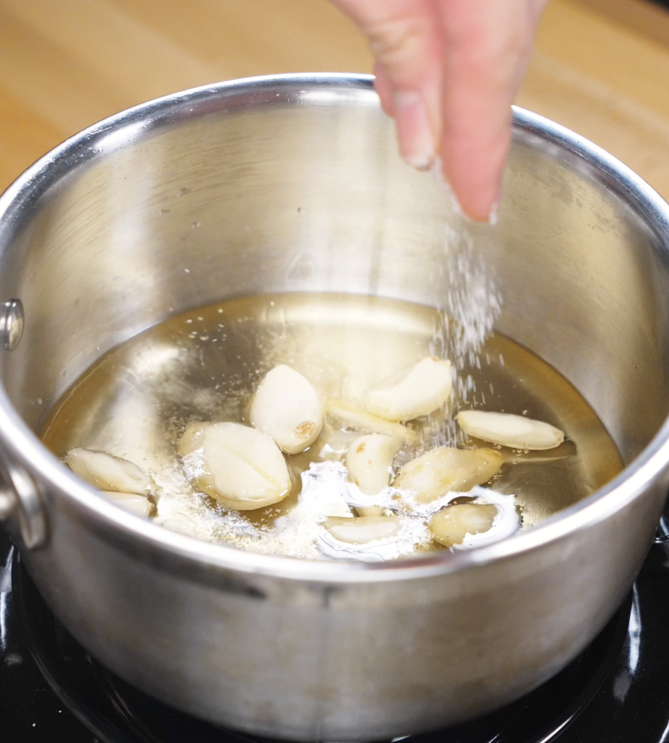 Whole garlic cloves sizzling in hot oil in a saucepan, infusing flavor for garlic roasted potatoes.