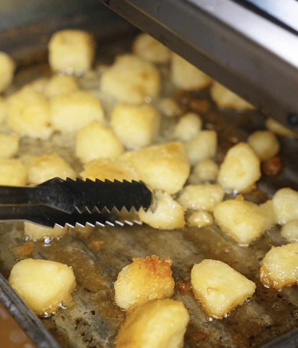 Tray of roughed-up potatoes coated in garlic oil being placed in the oven, ready to roast to golden perfection.