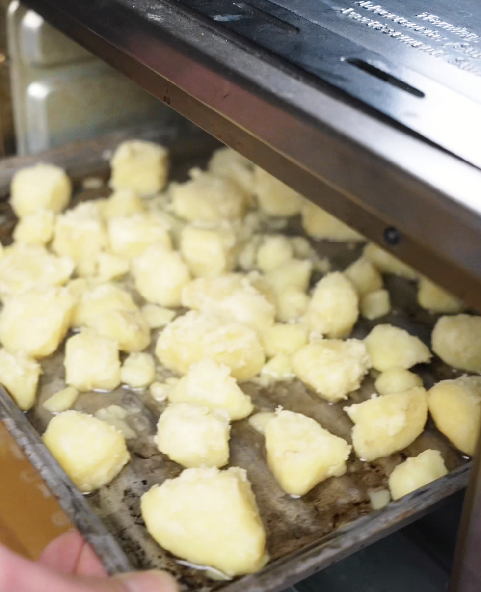 Fluffed and roughed-up boiled potatoes in a mixing bowl, prepped for ultimate crispiness in the oven.