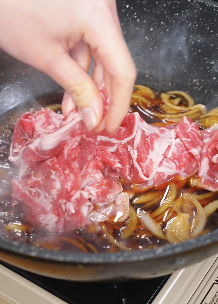 Adding thinly sliced ribeye beef into the simmering gyudon broth with softened onions to cook gently until tender.