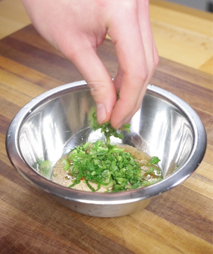 Finely chopped cilantro being added to a bowl of Crying Tiger Steak sauce to build a fresh, herbal flavor.