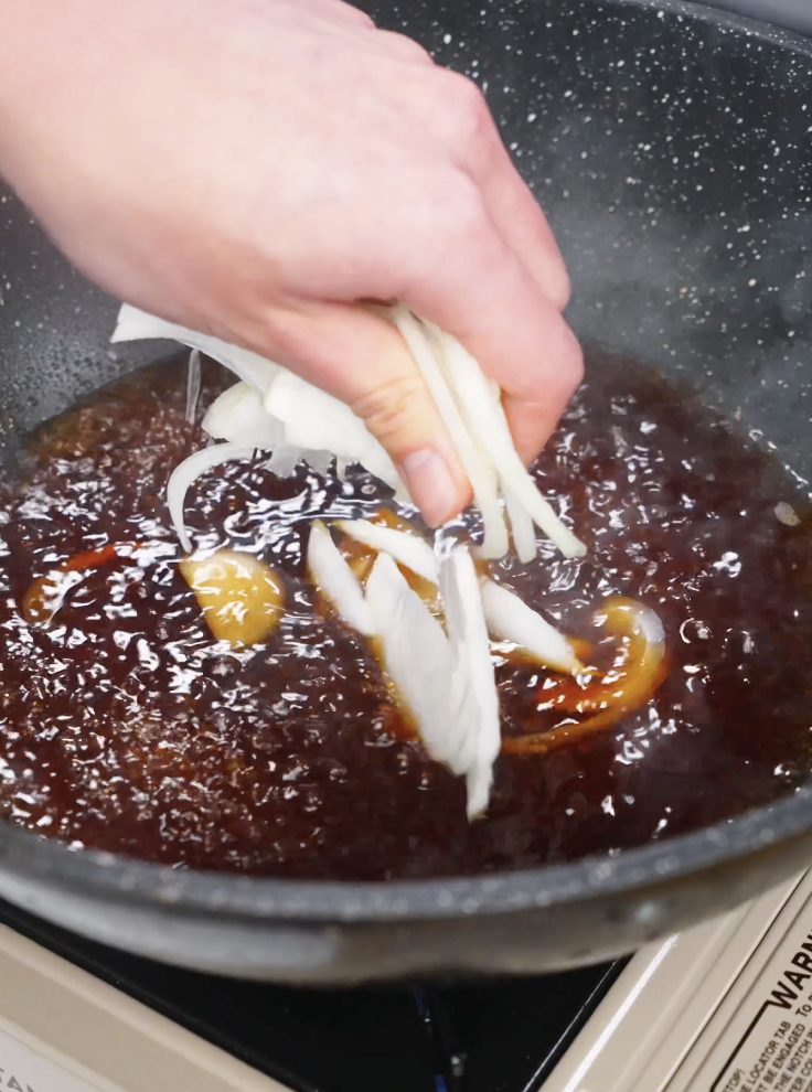 Adding thinly sliced onions into a simmering gyudon broth made with dashi, soy sauce, sake, mirin, and sugar.