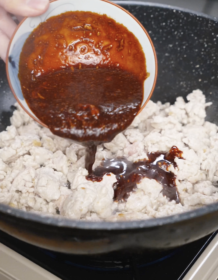 Thick peanut gochujang sauce being poured over cooked ground chicken in a pan to create a creamy and spicy Spicy Peanut Chicken sauce.
