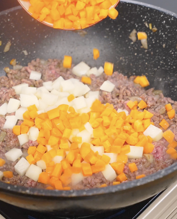 Diced potatoes and carrots being added to browned ground beef in a pan, preparing the vegetable base for Japanese ground beef curry.