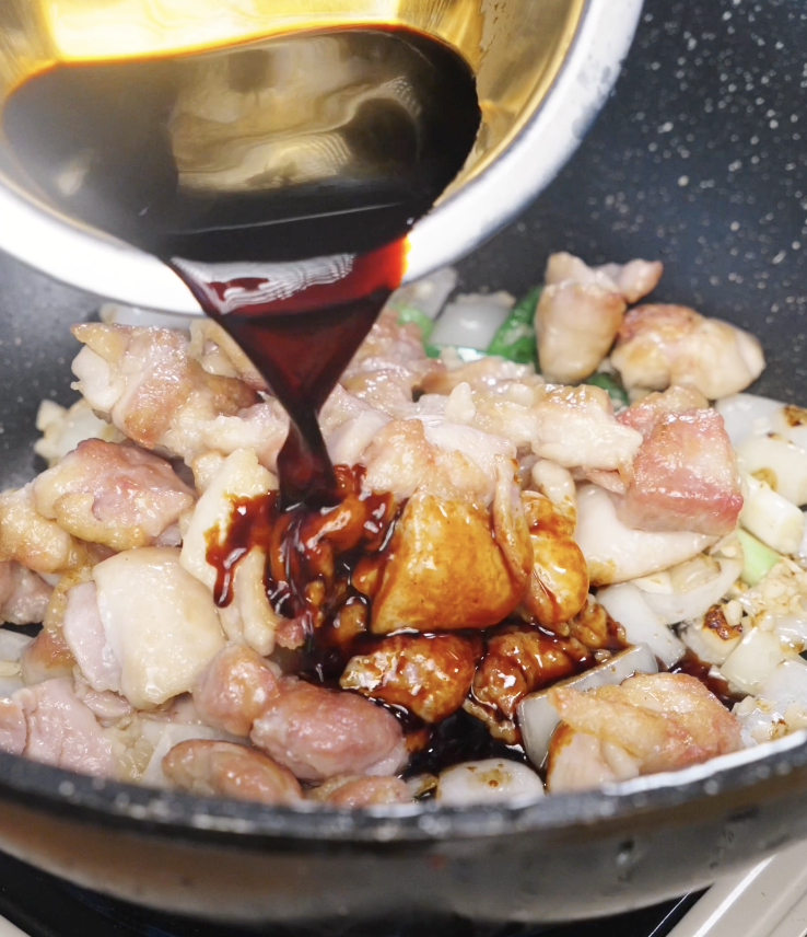Pouring prepared soy garlic sauce over browned chicken and aromatics as it begins to thicken and coat the stir fry.