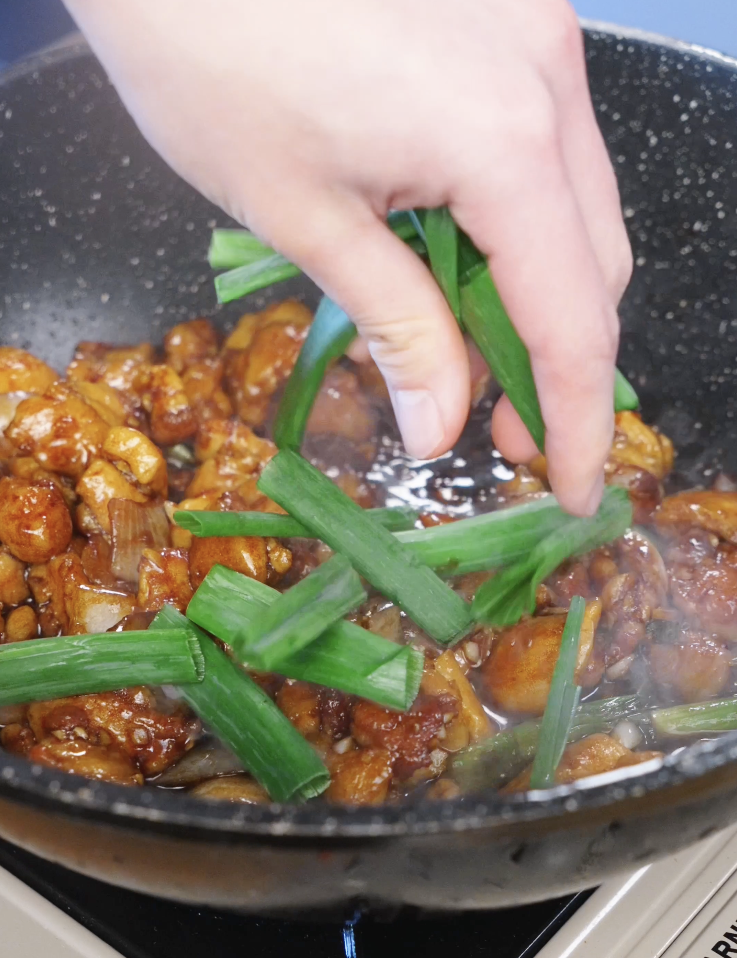 Adding sliced scallion greens to the garlic chicken stir fry as the final step before serving.