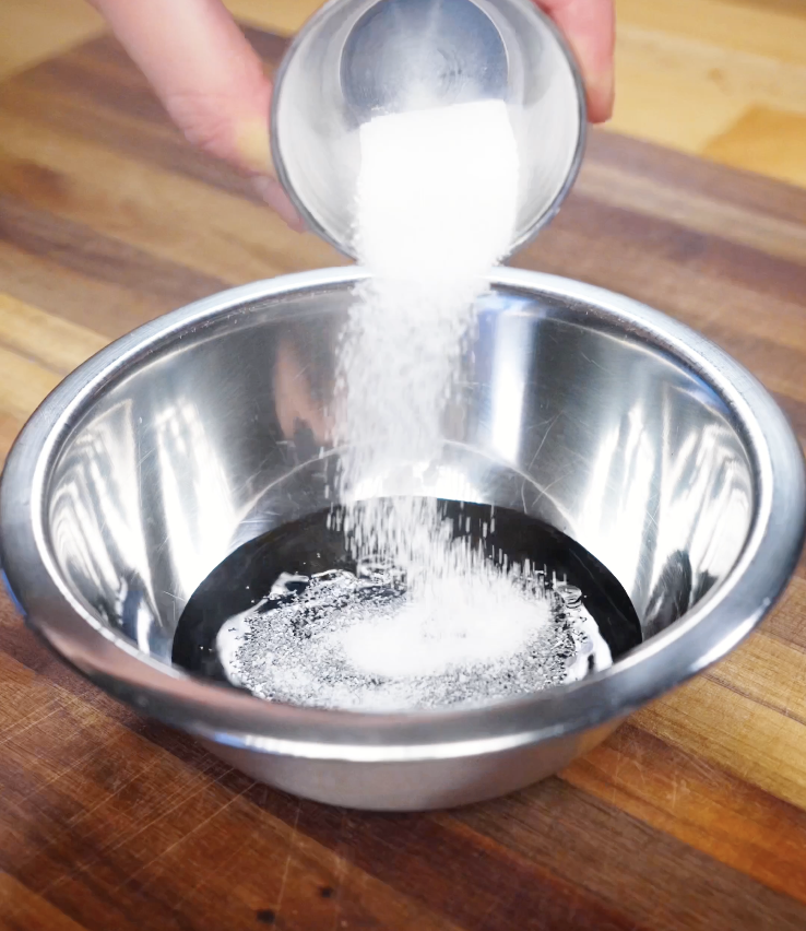 Granulated sugar being poured into a bowl of dark soy sauce, light soy sauce, and fish sauce to create the sweet and savory Pad Kra Pao sauce.