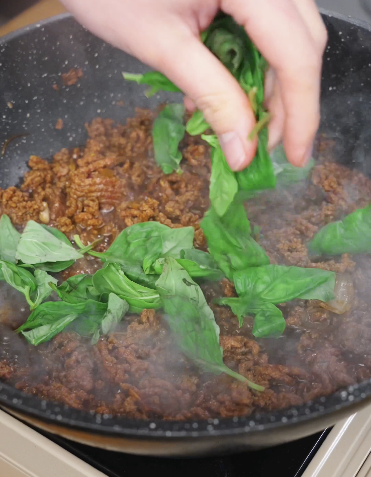 Fresh Thai basil leaves being tossed into the cooked Pad Kra Pao beef just before serving, adding fragrance and freshness.