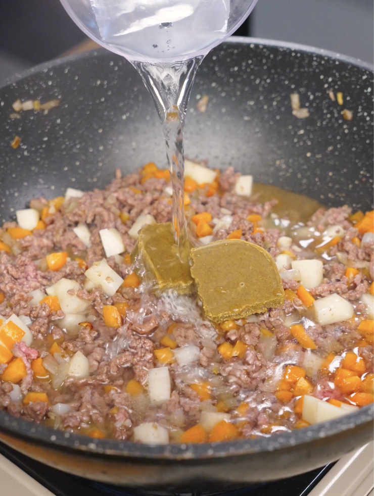 Water being poured into the pan with ground beef, vegetables, and Japanese curry blocks as the sauce begins to form.