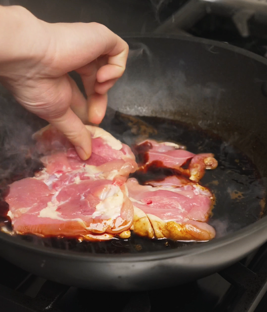Skin-on chicken thighs being gently placed into the simmering soy sauce braising liquid, beginning the cooking process for tender soy sauce chicken.