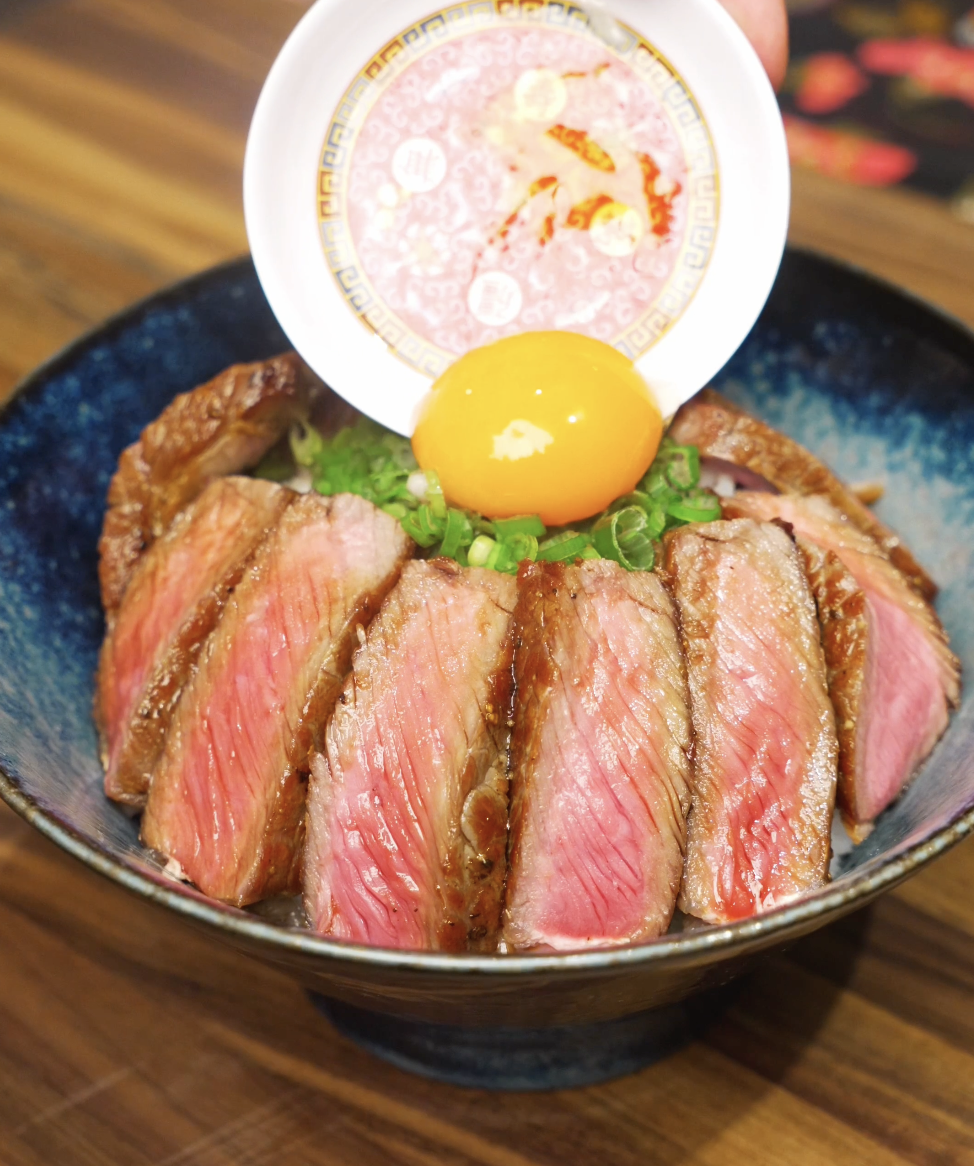 A raw egg yolk being gently placed on top of sliced steak and scallions for a rich finish to the Japanese steak bowl.
