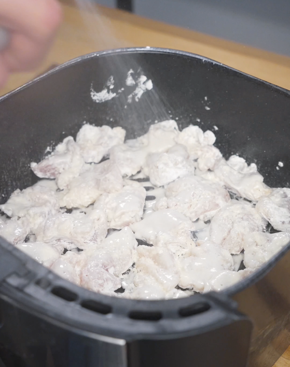 Cornstarch-coated chicken pieces arranged in a single layer inside an air fryer basket, lightly sprayed with oil before cooking to achieve a crispy texture without deep frying.