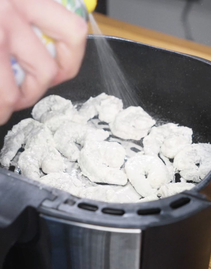 Cornstarch-coated shrimp arranged in an air fryer basket and lightly sprayed with oil before air frying until crispy for Bang Bang Shrimp.
