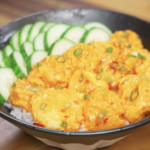 Finished bowl of Bang Bang Shrimp made with crispy air-fried shrimp coated in a creamy sweet-spicy bang bang sauce, served over steamed rice with sliced cucumbers and scallions as a healthy Asian dinner.