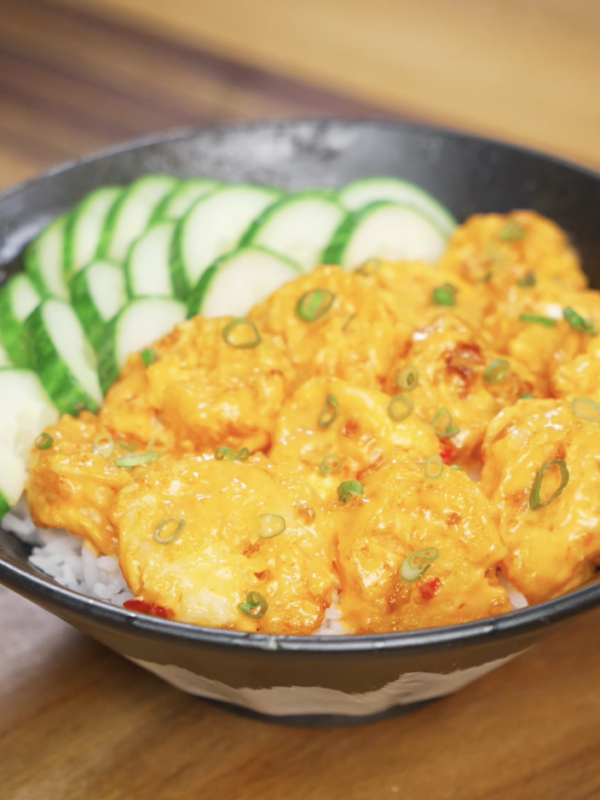 Finished bowl of Bang Bang Shrimp made with crispy air-fried shrimp coated in a creamy sweet-spicy bang bang sauce, served over steamed rice with sliced cucumbers and scallions as a healthy Asian dinner.