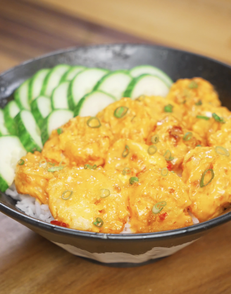 Finished bowl of Bang Bang Shrimp made with crispy air-fried shrimp coated in a creamy sweet-spicy bang bang sauce, served over steamed rice with sliced cucumbers and scallions as a healthy Asian dinner.