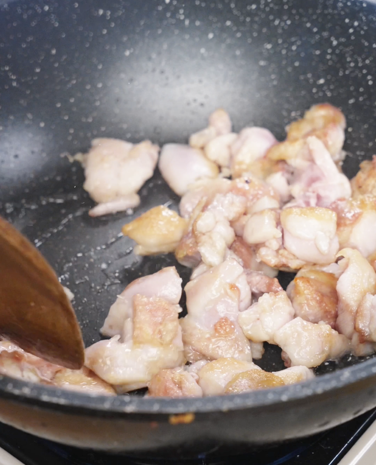 Chicken thigh pieces browning in a nonstick pan to develop flavor before being tossed with garlic and vegetables.