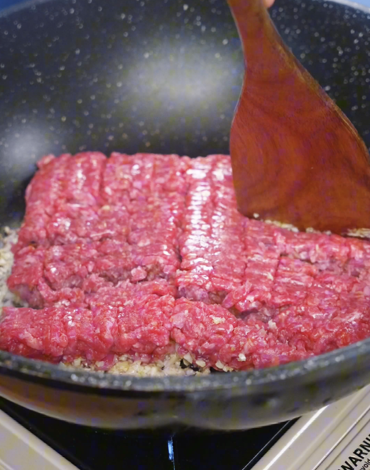 Ground beef added to a pan over saut&eacute;ed garlic and ginger, beginning to brown before being broken apart for Korean BBQ beef.