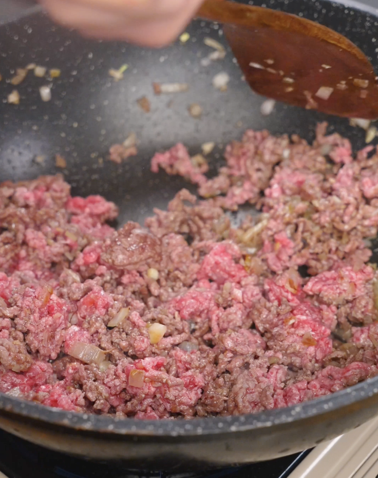 Ground beef cooking in a pan with saut&eacute;ed onions, partially browned and broken apart for an easy weeknight Japanese curry.