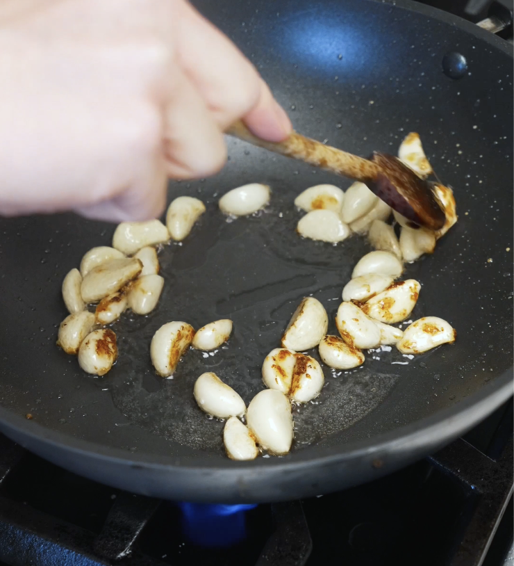 Whole garlic cloves cooking in oil in a pan until golden and lightly caramelized.