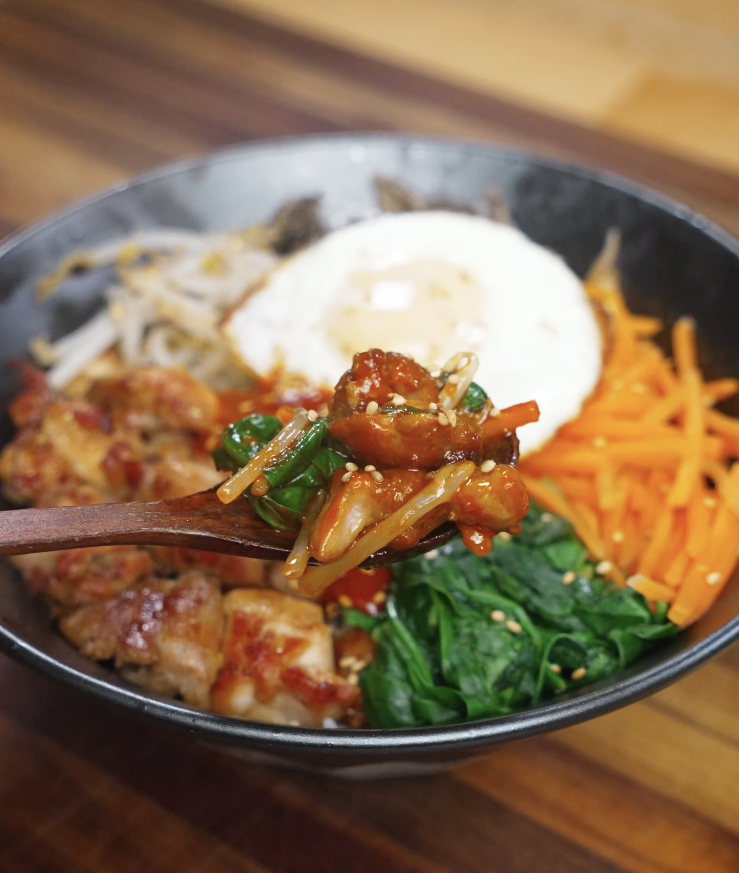 Close-up spoonful of chicken bibimbap showing marinated chicken, vegetables, gochujang sauce, and rice mixed together for a flavorful bite.