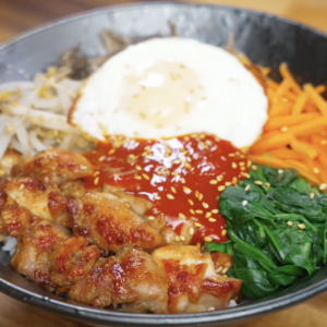 Finished chicken bibimbap bowl with marinated chicken thighs, steamed vegetables, gochujang sauce, and a fried egg served over rice as a balanced healthy Asian dinner.