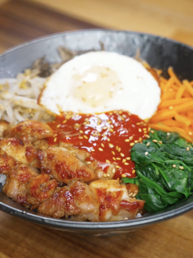 Finished chicken bibimbap bowl with marinated chicken thighs, steamed vegetables, gochujang sauce, and a fried egg served over rice as a balanced healthy Asian dinner.