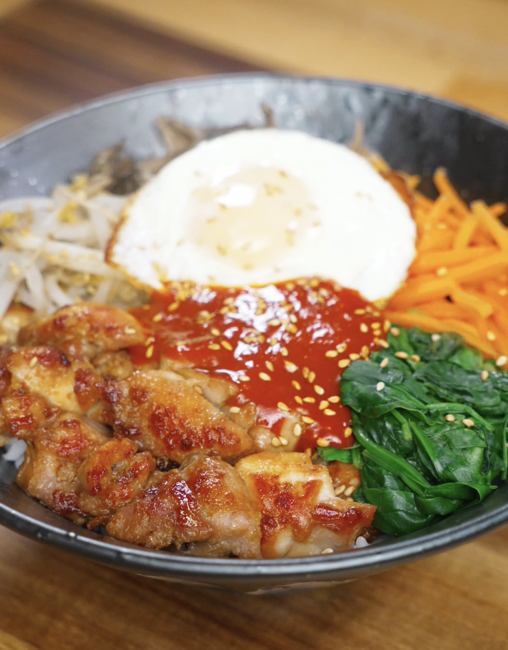 Finished chicken bibimbap bowl with marinated chicken thighs, steamed vegetables, gochujang sauce, and a fried egg served over rice as a balanced healthy Asian dinner.