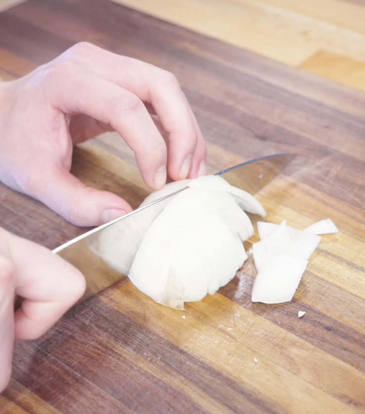 Slicing a white onion into thick wedges on a wooden cutting board to prepare vegetables for garlic chicken stir fry.