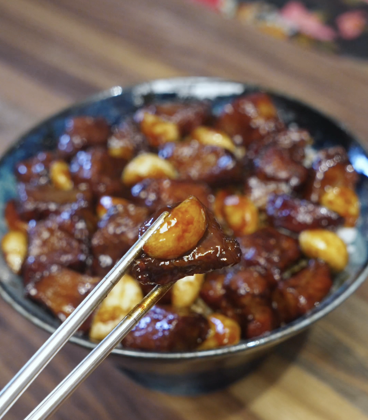 Chopsticks lifting a piece of tender steak and caramelized garlic coated in a savory black pepper sauce above a bowl of garlic steak stir fry.