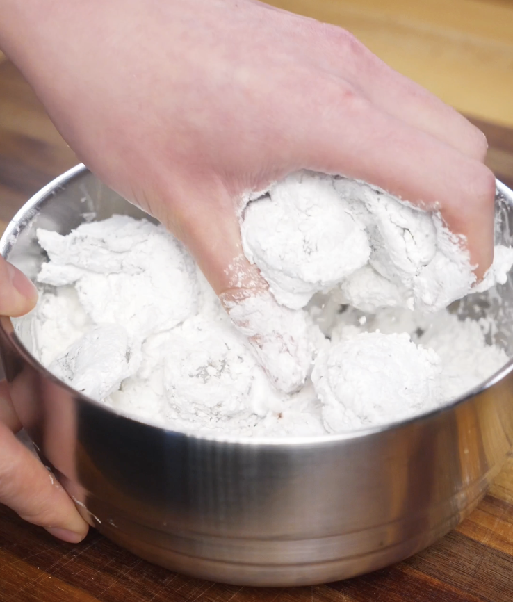 Shrimp being tossed in cornstarch and salt in a stainless steel bowl to create a light, crispy coating before air frying for Bang Bang Shrimp.