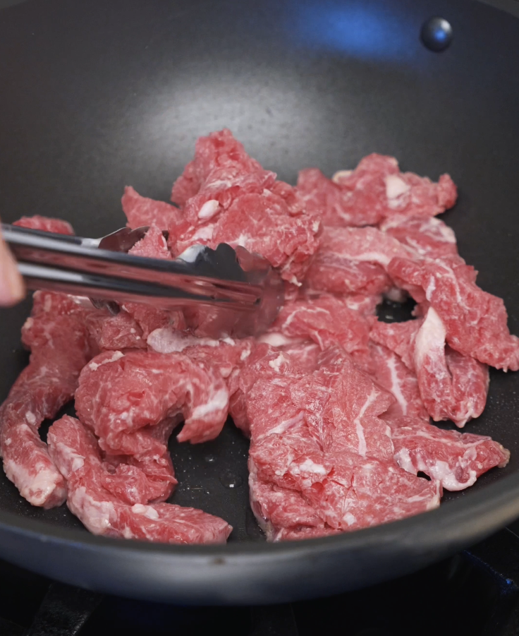 Thinly sliced beef cooking in a hot pan, searing quickly over high heat to build flavor for beef and broccoli.
