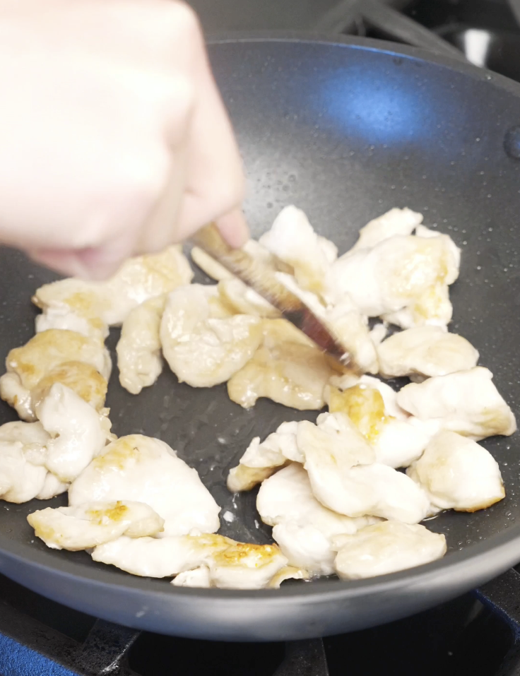 Thinly sliced chicken breast cooking in a nonstick pan until lightly golden and mostly cooked through for string bean chicken.