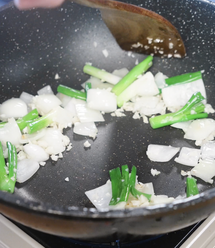 Saut&eacute;ing minced garlic, onion wedges, and scallion whites in a pan to build the aromatic base for garlic chicken stir fry.