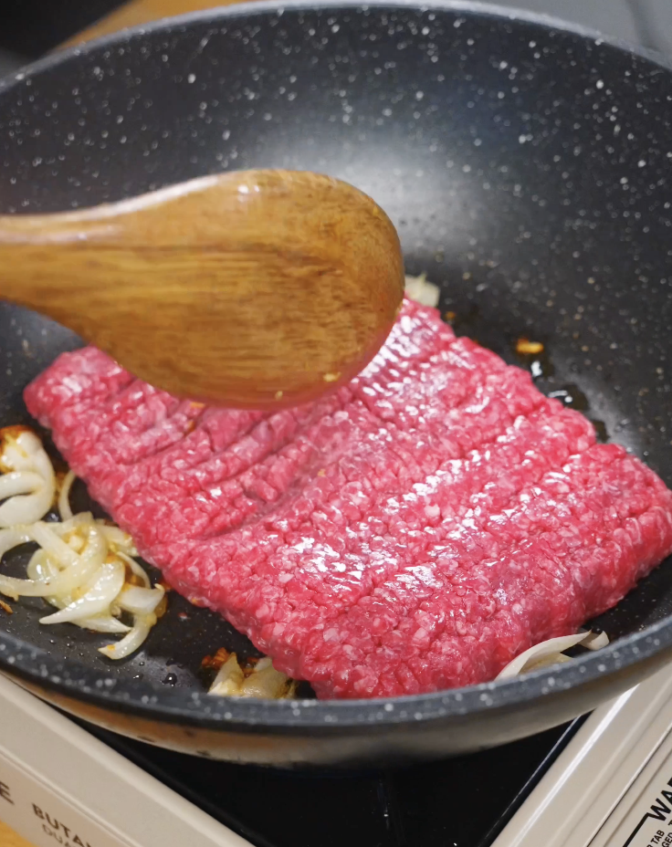 Lean ground beef added to a pan with saut&eacute;ed onions and aromatics, beginning to brown for Pad Kra Pao.