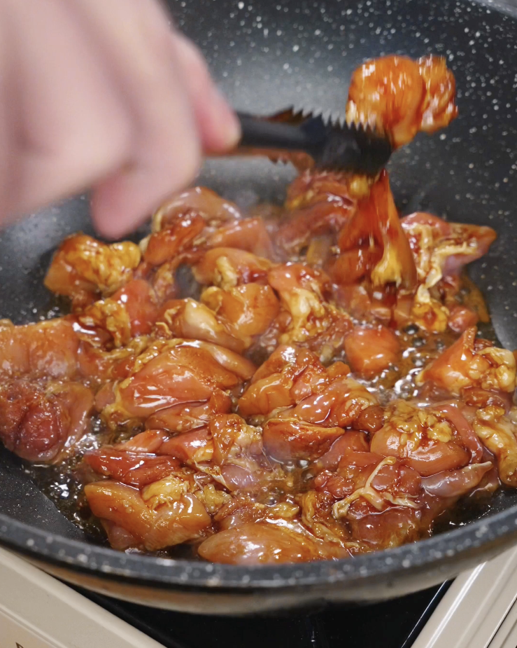 Honey garlic chicken thighs cooking in a pan as the sauce bubbles and reduces into a sticky glaze, creating caramelized edges on the chicken during stovetop cooking.